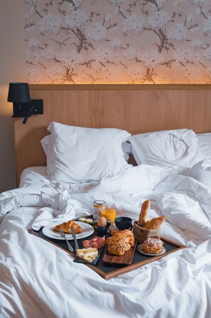 Un lit bien fait, avec du linge de lit blanc, un plateau contenant des éléments de petit-déjeuner, notamment des croissants, un croissant sur une assiette et un verre de jus d’orange.