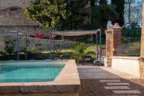 Une piscine bordée de pierres, une pergola et un mur de briques en arrière-plan.