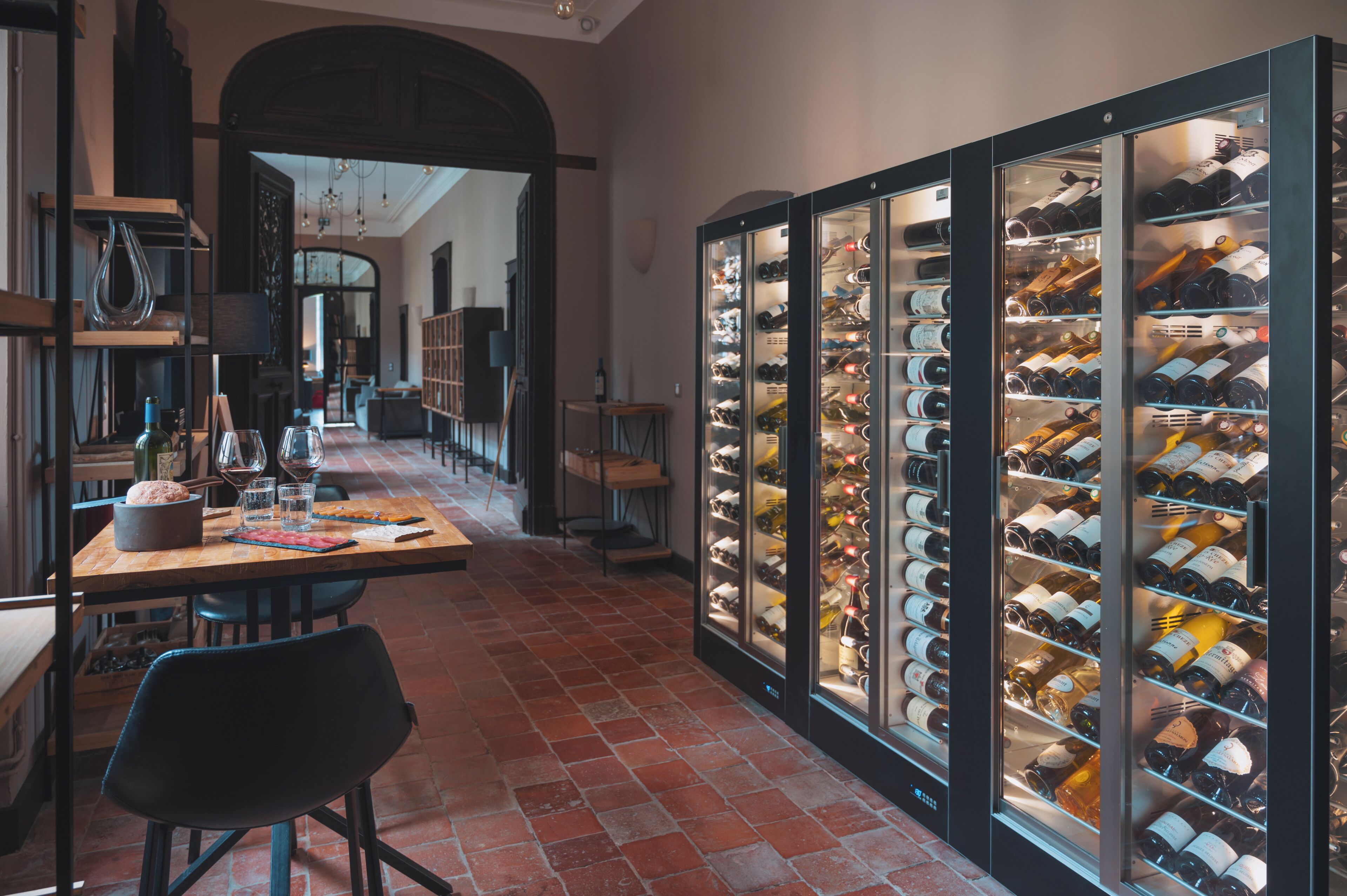 Una bodega con estantes llenos de botellas de vino, un comedor con una mesa y sillas, y un suelo de ladrillo.