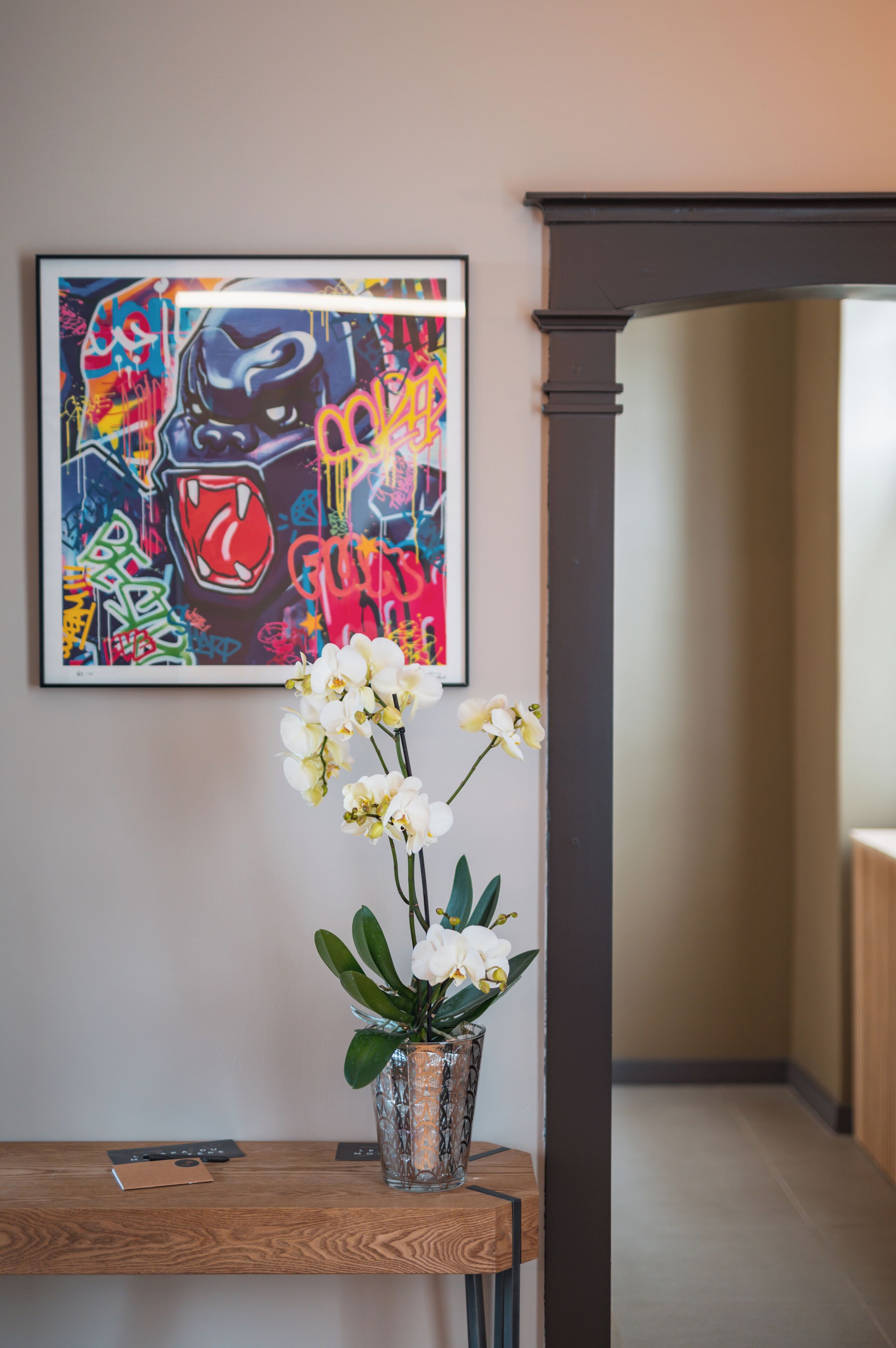 A framed artwork on the wall, a vase with white orchids, and a wooden table with a remote control.