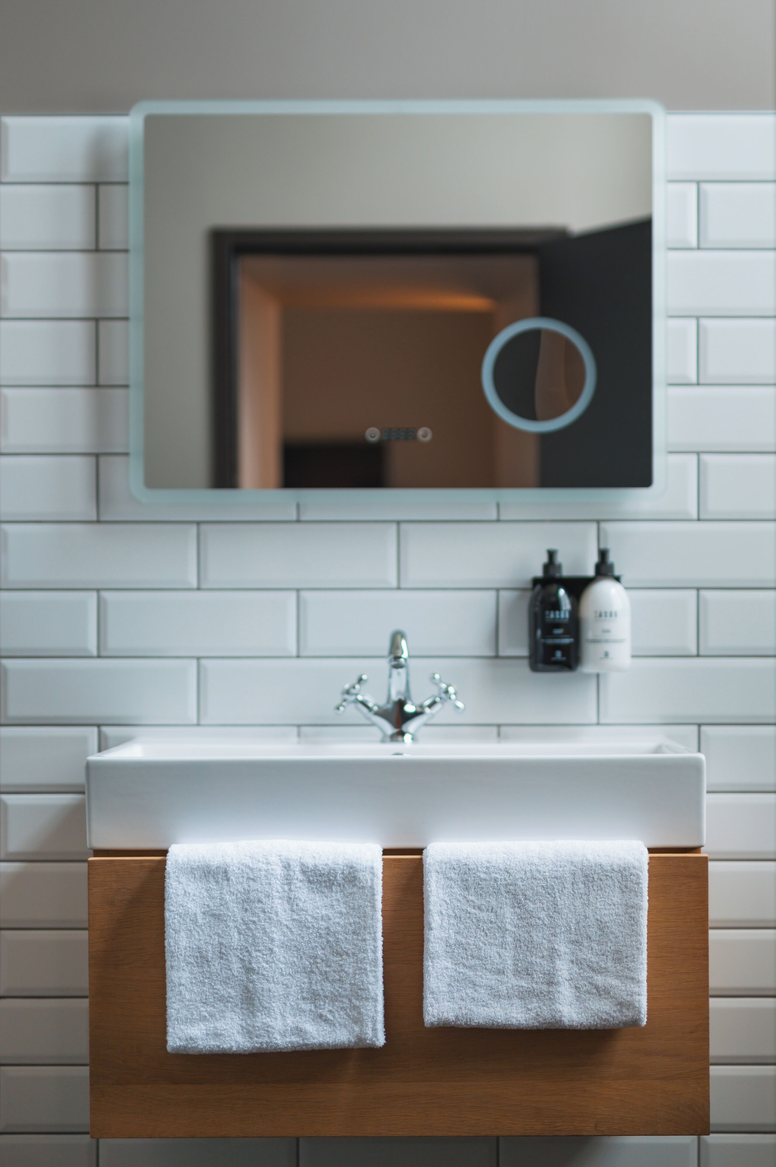 Une salle de bain avec un lavabo blanc, deux serviettes, un miroir et deux flacons de savon pour les mains.