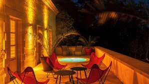 Eine Terrasse im Freien mit roten Stühlen und einem Whirlpool, umgeben von Topfpflanzen und einer Steinmauer.