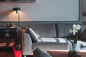 Un salon moderne avec un canapé gris, un panier rouge, une lampe sur pied et un vase contenant des fleurs blanches.