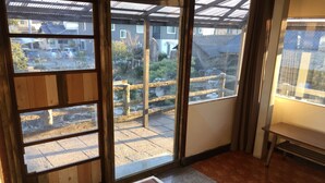 Una habitación con piso de madera, una banca y vista a un patio con muro de piedra y cerca de madera.