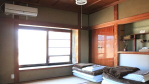 Una habitación con suelo de tatami, un ventanal grande, un armario de madera y una estantería con adornos.