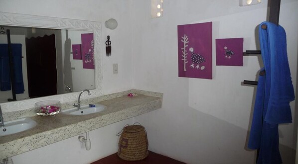 A bathroom with two sinks, a mirror, and wall-mounted artwork. - Kusini Beach Cottages (Diani Beach)