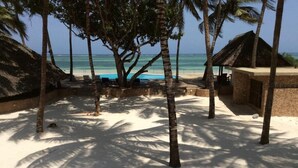 A beach with palm trees, a thatched-roof hut, and a pool area. - Kusini Beach Cottages (Diani Beach)