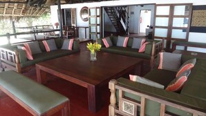 A room with a wooden table, green cushioned seating, a hanging light fixture, and a staircase leading to an upper level. - Kusini Beach Cottages (Diani Beach)