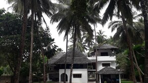 A resort with a white building, thatched-roof structures, and palm trees. - Kusini Beach Cottages (Diani Beach)