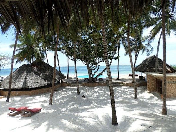 A beach with thatched-roof huts, palm trees, and sun loungers.
