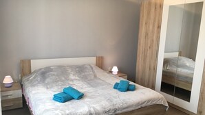 A bedroom with a large bed, wooden headboard, bedside lamps, and a wardrobe with a mirror. - Apartment Kumicic (Opatija)