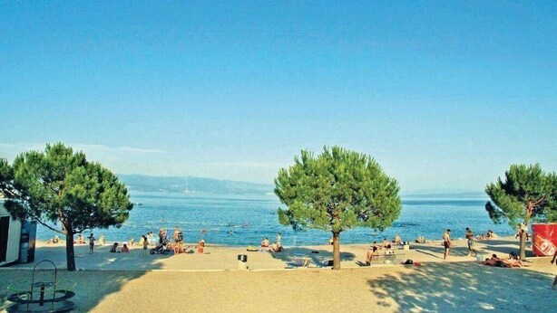 A beach with people relaxing, trees, and a clear view of the sea. - Apartment Kumicic (Opatija)