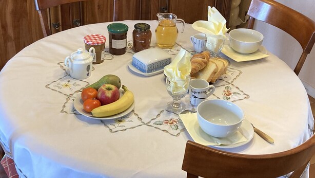 A breakfast table with a variety of food items including fruits, bread, and beverages. - CHAMBRE D'HÔTE CONFORTABLE (Voisins-le-Bretonneux)