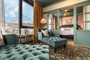 Una habitación con un ventanal grande, una cama, un sofá tapizado en verde y una mesita de noche con una lámpara.