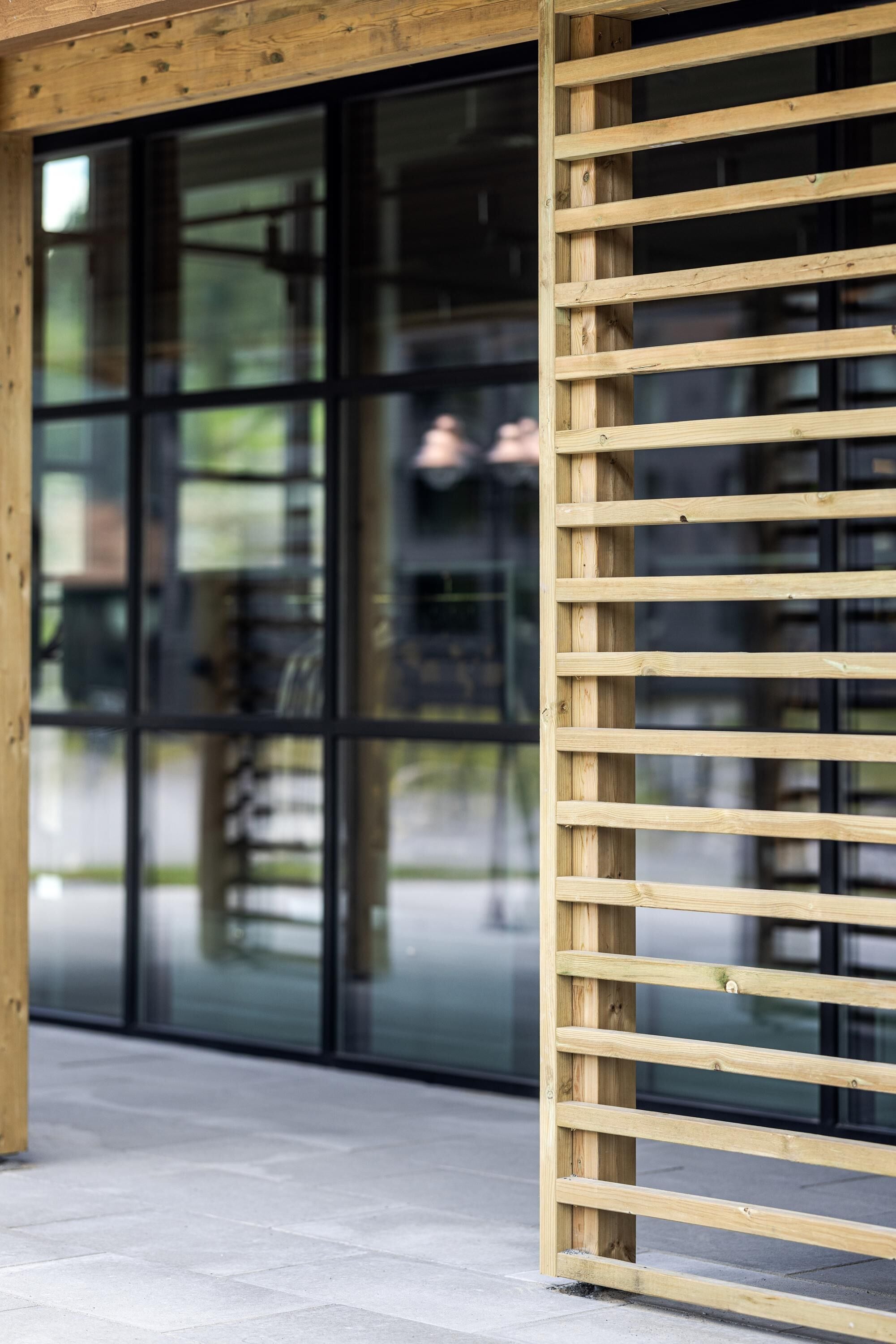 Une structure en bois composée de lattes, située à côté d’une porte vitrée, et qui fait probablement partie de l’extérieur d’un bâtiment.