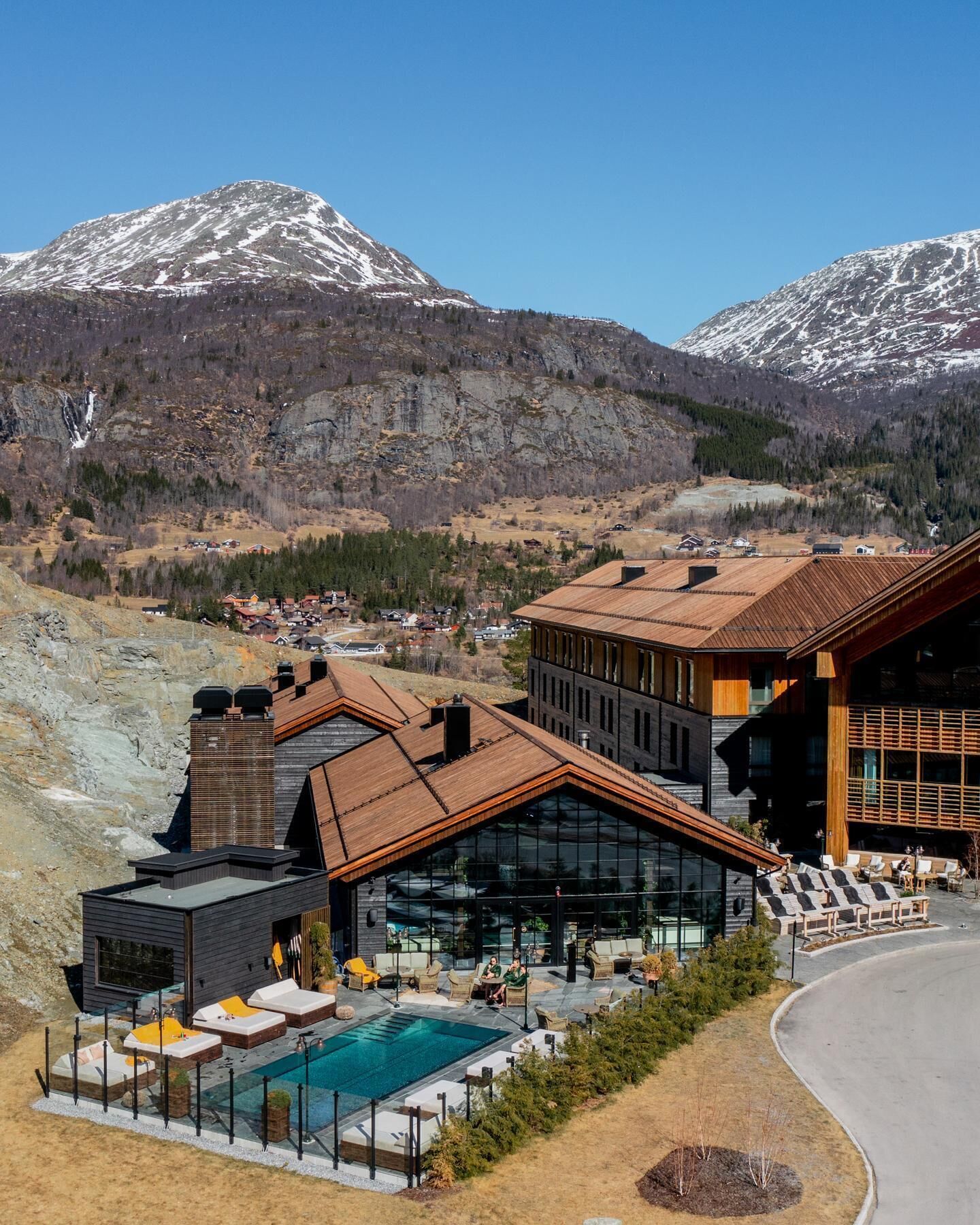 A modern hotel with a pool, large windows, and a view of snow-capped mountains.