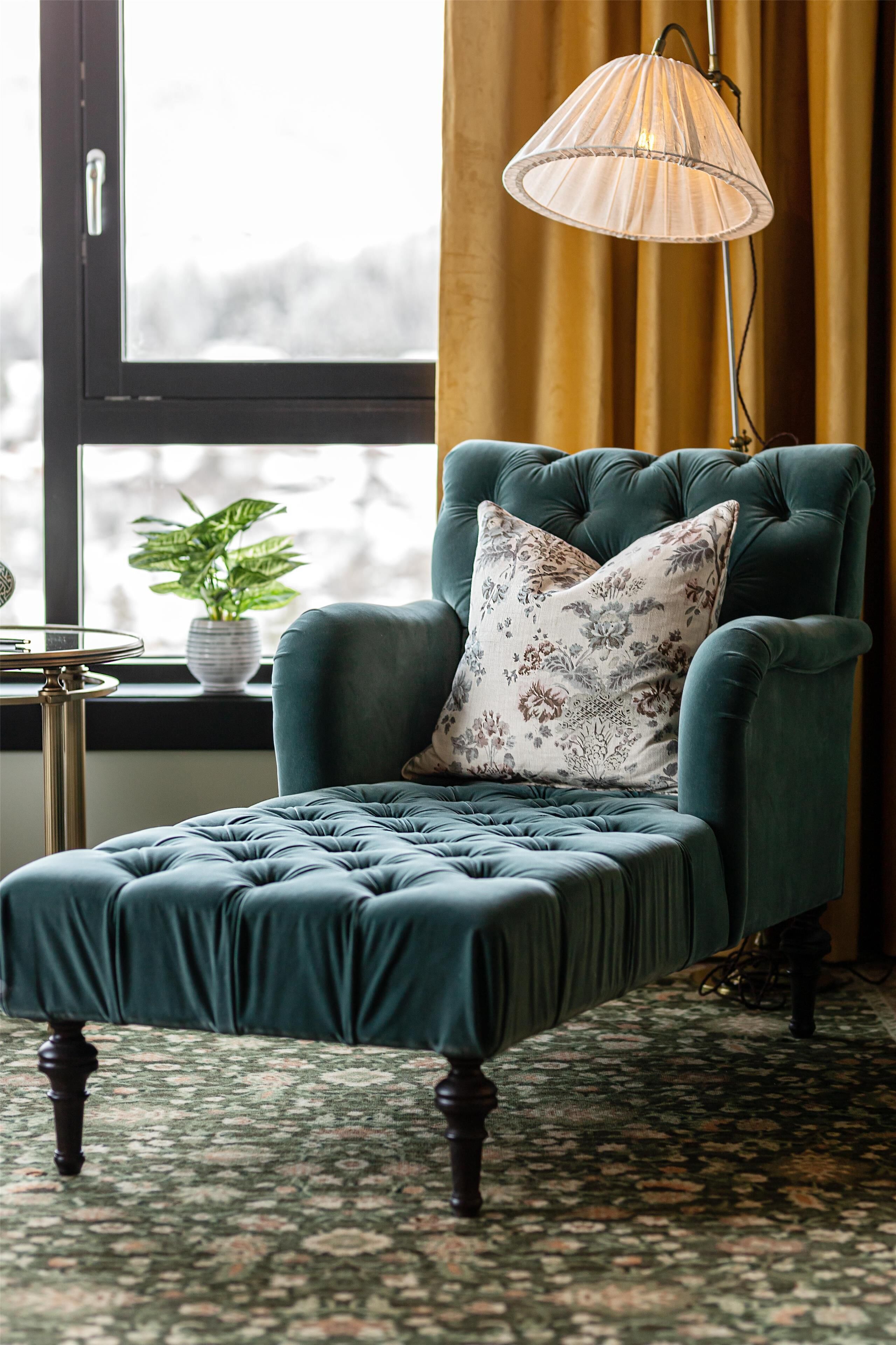 Un sillón color turquesa con un cojín estampado, una mesita auxiliar con una planta en maceta y una lámpara de pie.