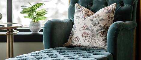 Un sillón color turquesa con un cojín estampado, una mesita auxiliar con una planta en maceta y una lámpara de pie.
