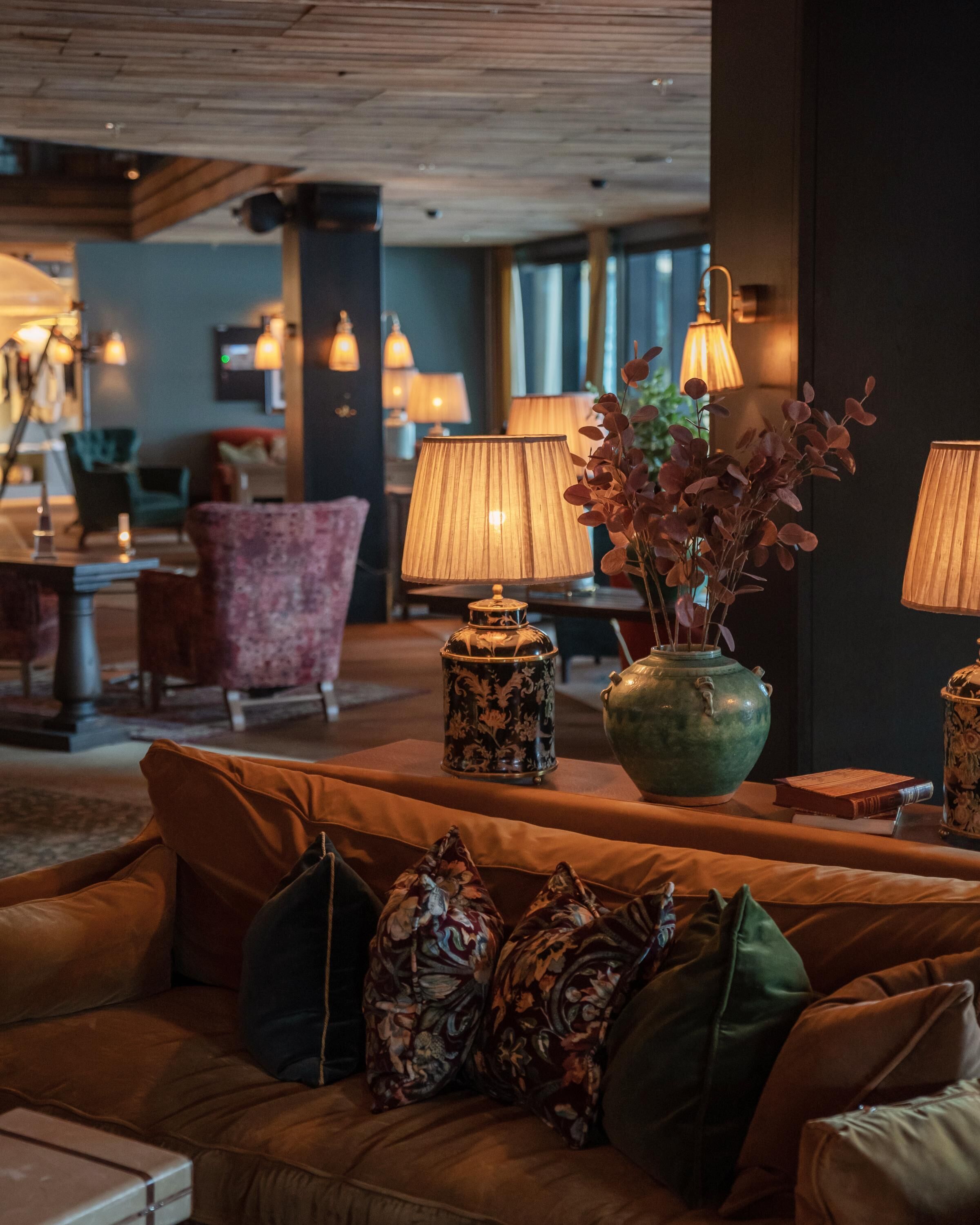 A cozy lounge area with a plush sofa, decorative lamps, and a vase with flowers.