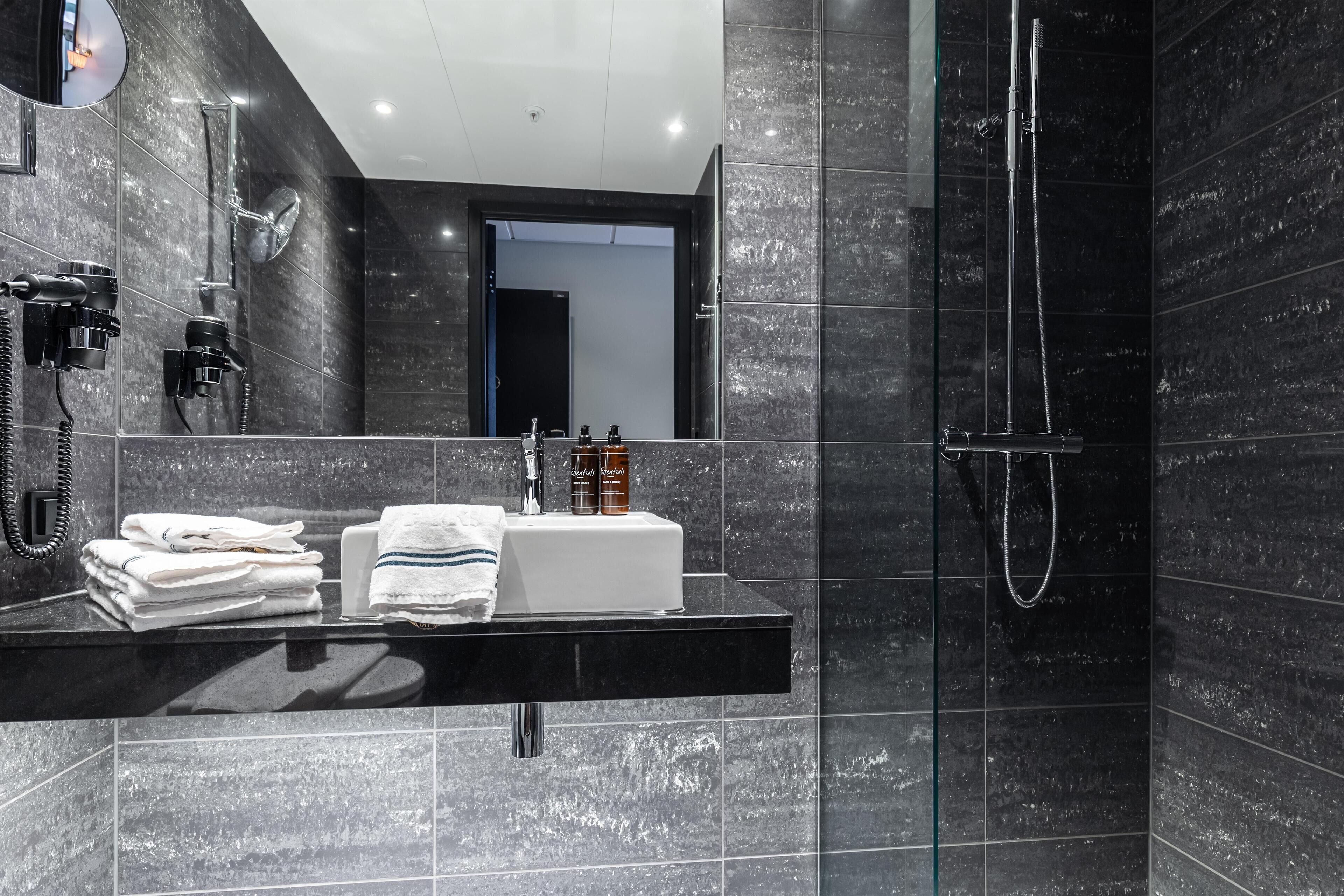 Un baño moderno con un lavamanos de mármol negro, una ducha con cerramiento de vidrio y un espejo grande.