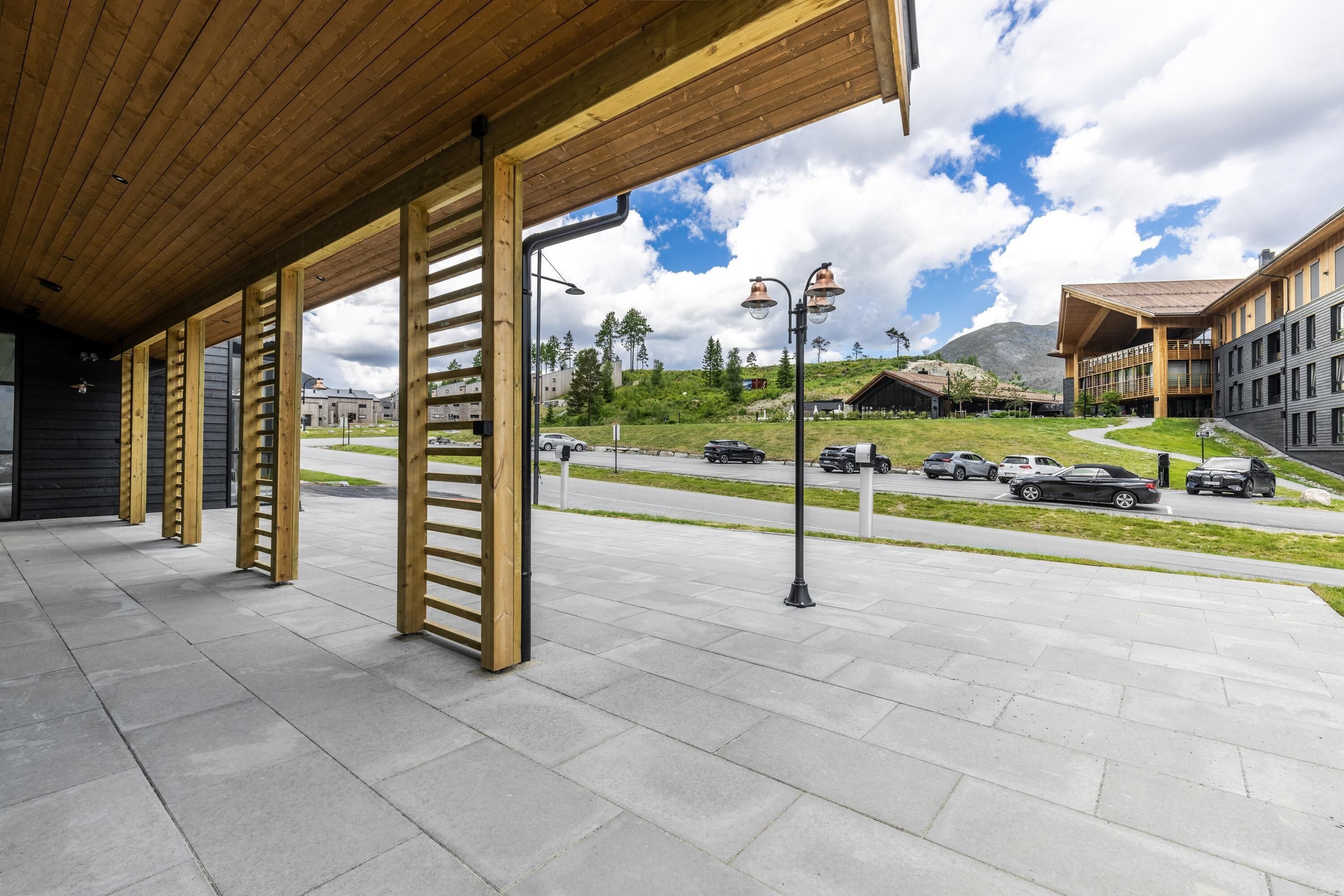 A covered outdoor area with a wooden ceiling, a paved walkway, and a view of a road with cars and buildings in the background.