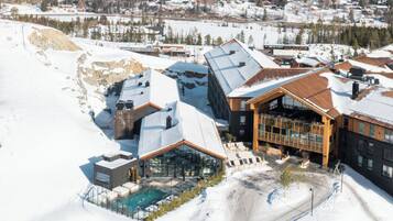 A modern ski resort with a glass-enclosed pool area, wooden cabins, and a ski lift visible in the background.