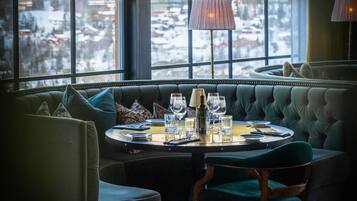 Un rincón acogedor con una mesa redonda dispuesta para comer, ventanas grandes con vista nevada y una lámpara sobre la mesa.