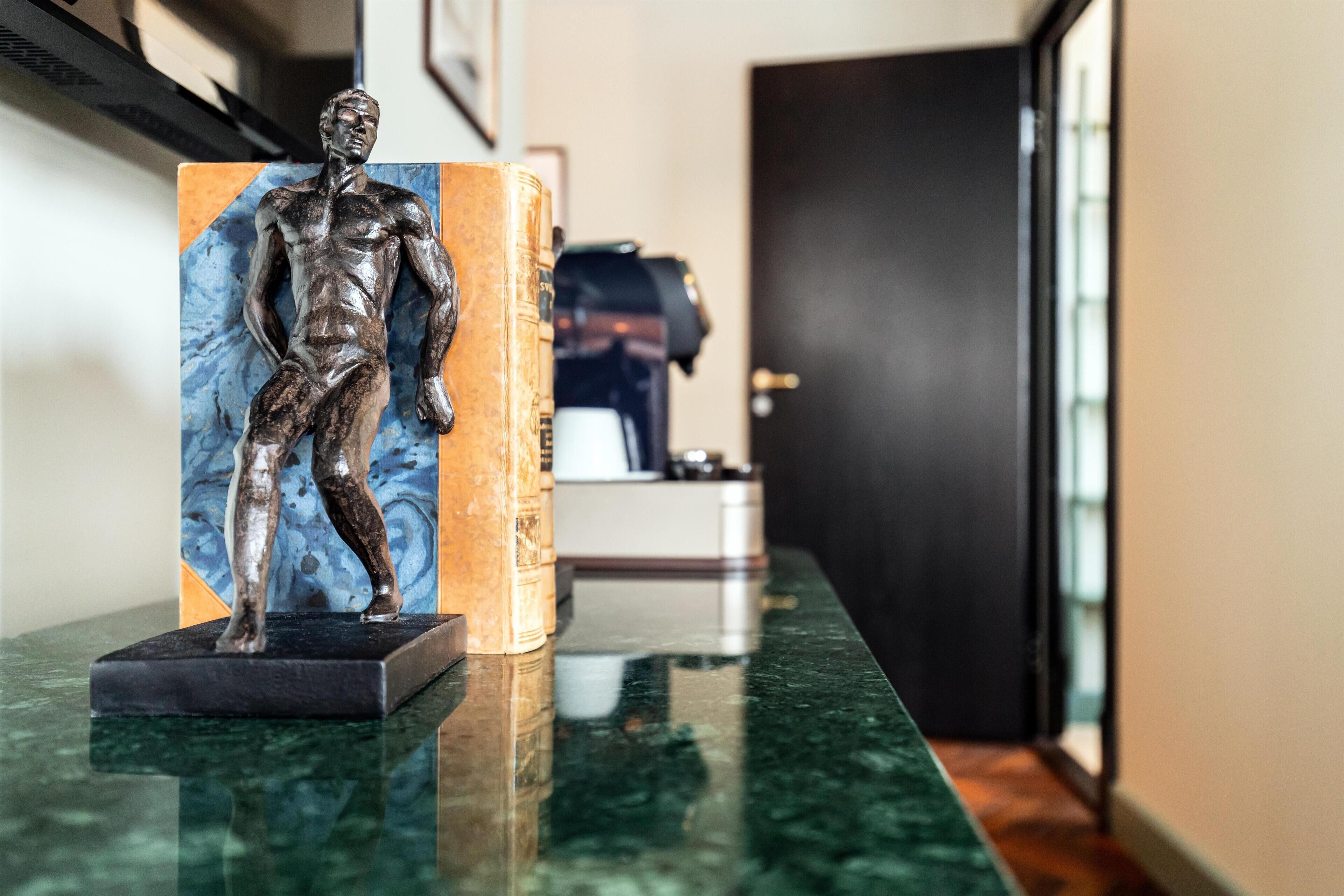 Une statue posée sur un comptoir en marbre, dans un couloir. On aperçoit une porte et un appareil à café à l’arrière-plan.