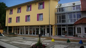 Een geel gebouw met roze luiken en een glazen ingang.