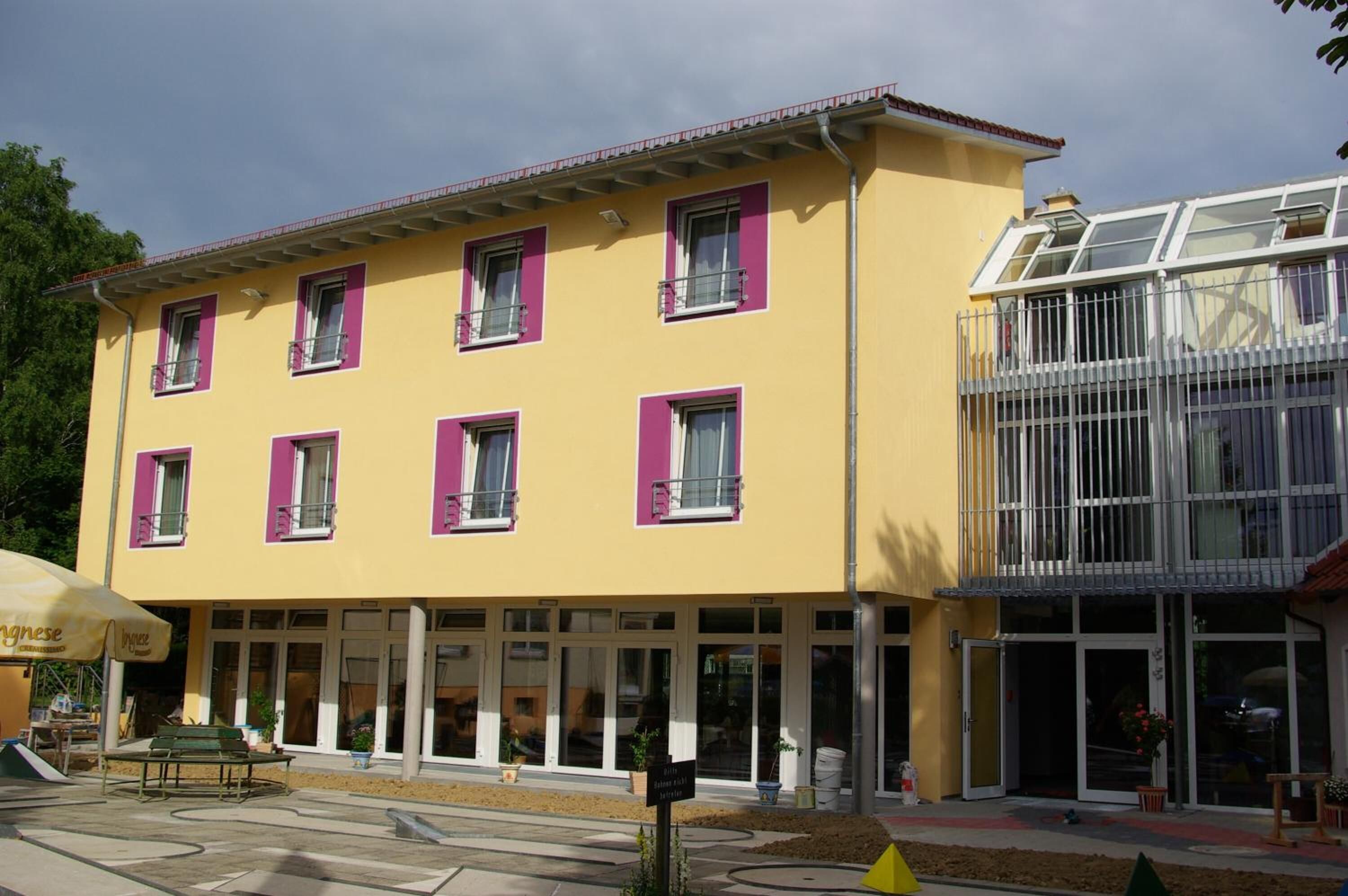 Ein gelbes Gebäude mit violetten Fensterläden, einem Glasbalkon und einem Café mit Außenbereich.