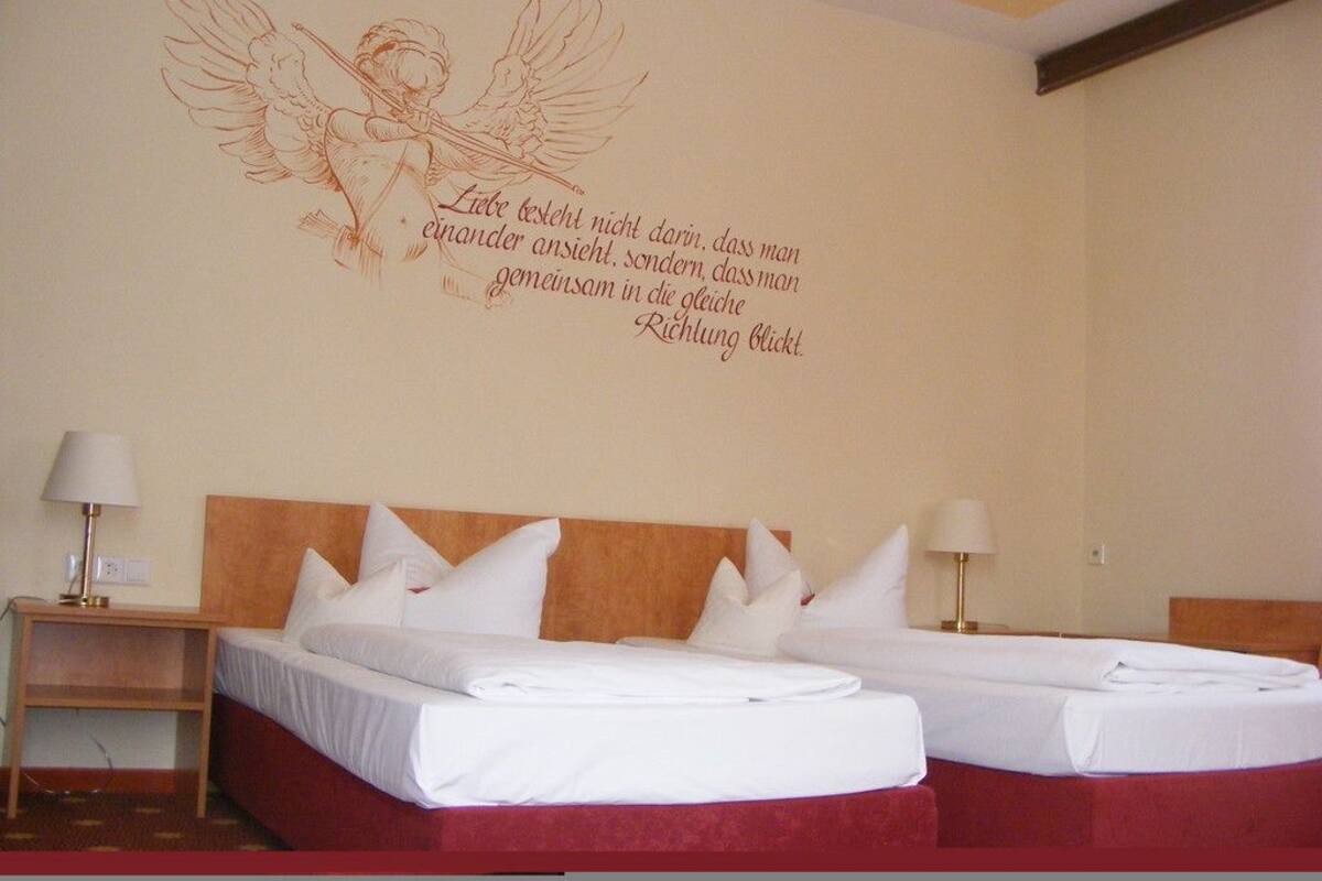 Habitación de hotel con dos camas, cabecero rojo y decoración de un ángel con alas.