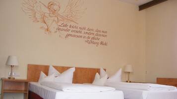 Ein Hotelzimmer mit zwei Betten, einem roten Kopfteil und einer Wanddekoration eines Engels mit Flügeln.