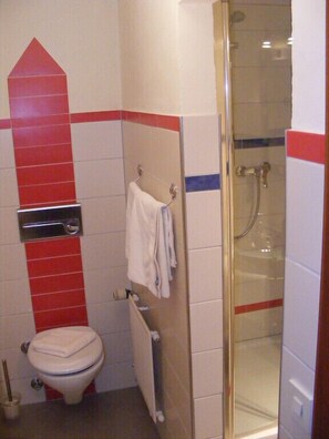 Casa de banho com sanita, toalheiro, chuveiro e radiador.
