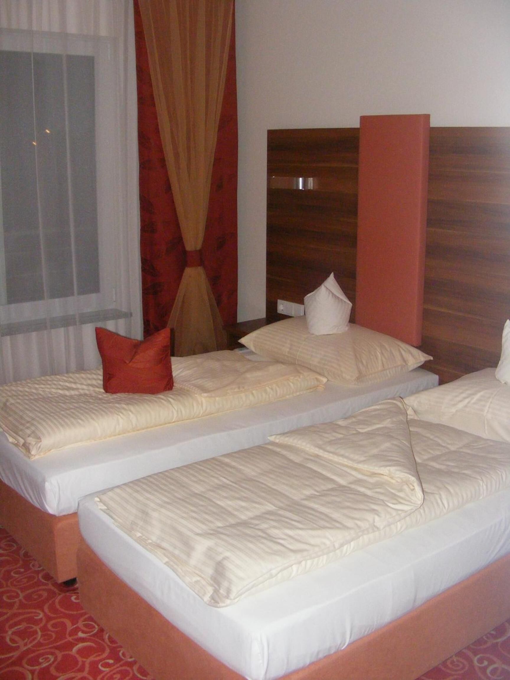 Ein Hotelzimmer mit zwei Einzelbetten, einem Holzkopfteil, einem roten Vorhang und einem gemusterten Teppich.