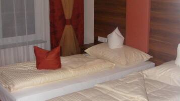 Ein Hotelzimmer mit zwei Einzelbetten, einem Holzkopfteil, einem roten Vorhang und einem gemusterten Teppich.