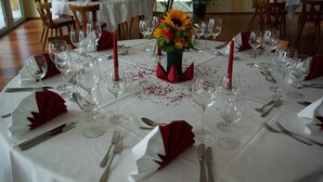 Een ronde eettafel gedekt voor een formeel evenement, met witte tafelkleden, rode servetten en een bloemenstuk als decoratie.