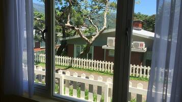 A window with a view of a white picket fence, a tree, and a building with a brick facade.