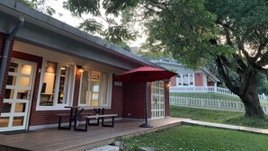 En murstensbygning med en overdækket terrasse, udendørs siddepladser og et hvidt stakitshegn.