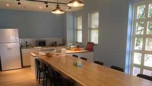 Et moderne køkken med et træspisebord, stole, et køleskab, en mikroovn og et vindue med persienner.