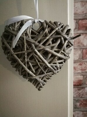 A heart-shaped decoration made of intertwined branches, tied with a white ribbon, hanging on a wall with a brick pattern. - Gruga Apartment an der Messe (Essen)