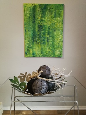 A glass table with a metal stand, a bowl containing decorative items, and a green abstract painting on the wall. - Gruga Apartment an der Messe (Essen)