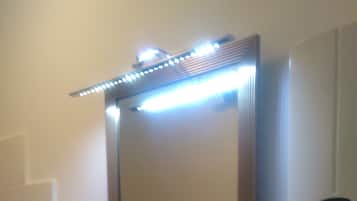 Ein Badezimmer mit einem weißen Waschbecken, einem Spiegel mit LED-Beleuchtung und einer digitalen Uhr an der Wand.