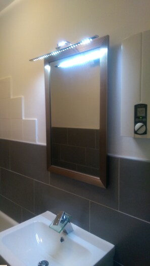 A bathroom with a white sink, a mirror with LED lights, and a digital clock on the wall. - Gruga Apartment an der Messe (Essen)
