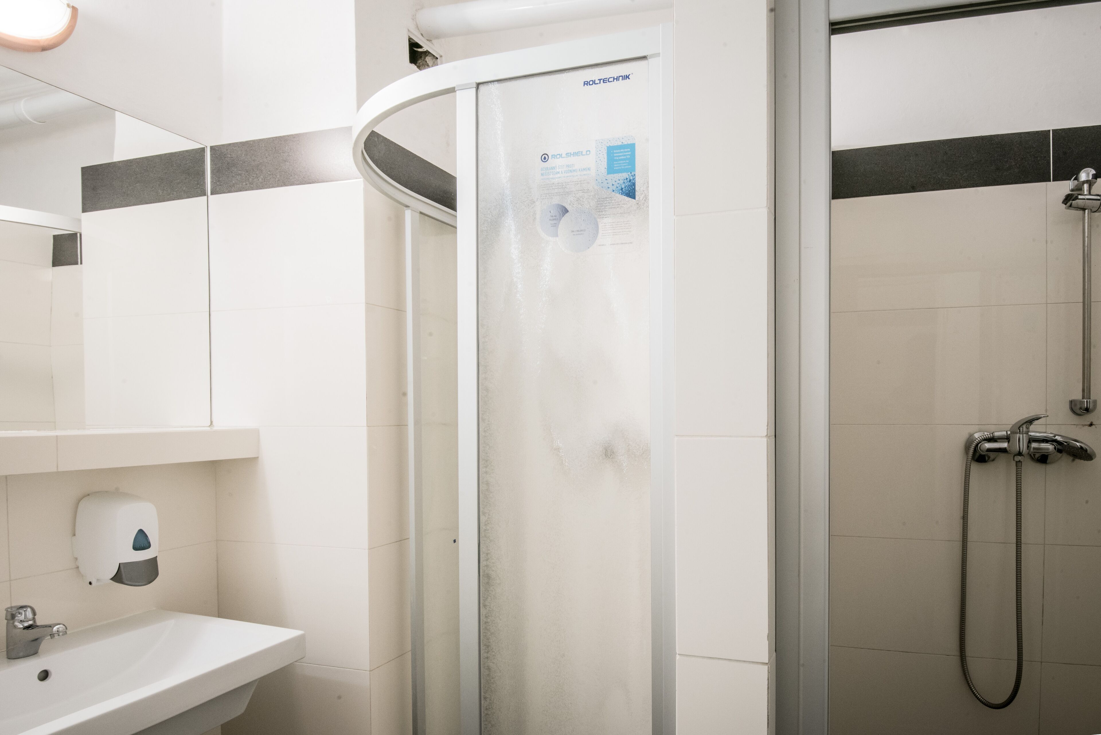 Un baño con ducha acristalada, lavamanos y dispensador de jabón.