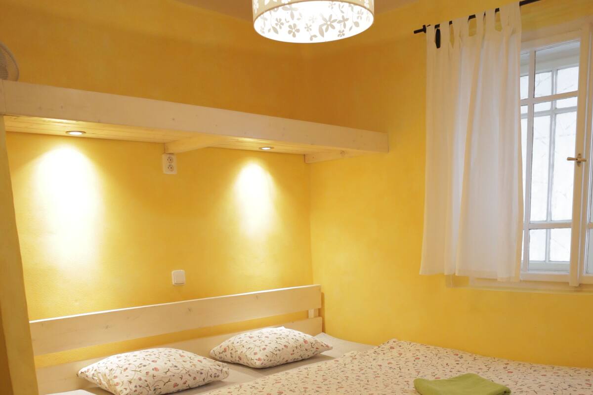 A single bed with a floral bedspread, two pillows, and a green towel.