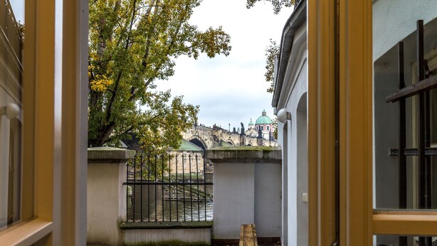 A courtyard with a bench, a stone bridge, and a building with a green dome in the background. - Charles Bridge Economic Hostel (Prague)