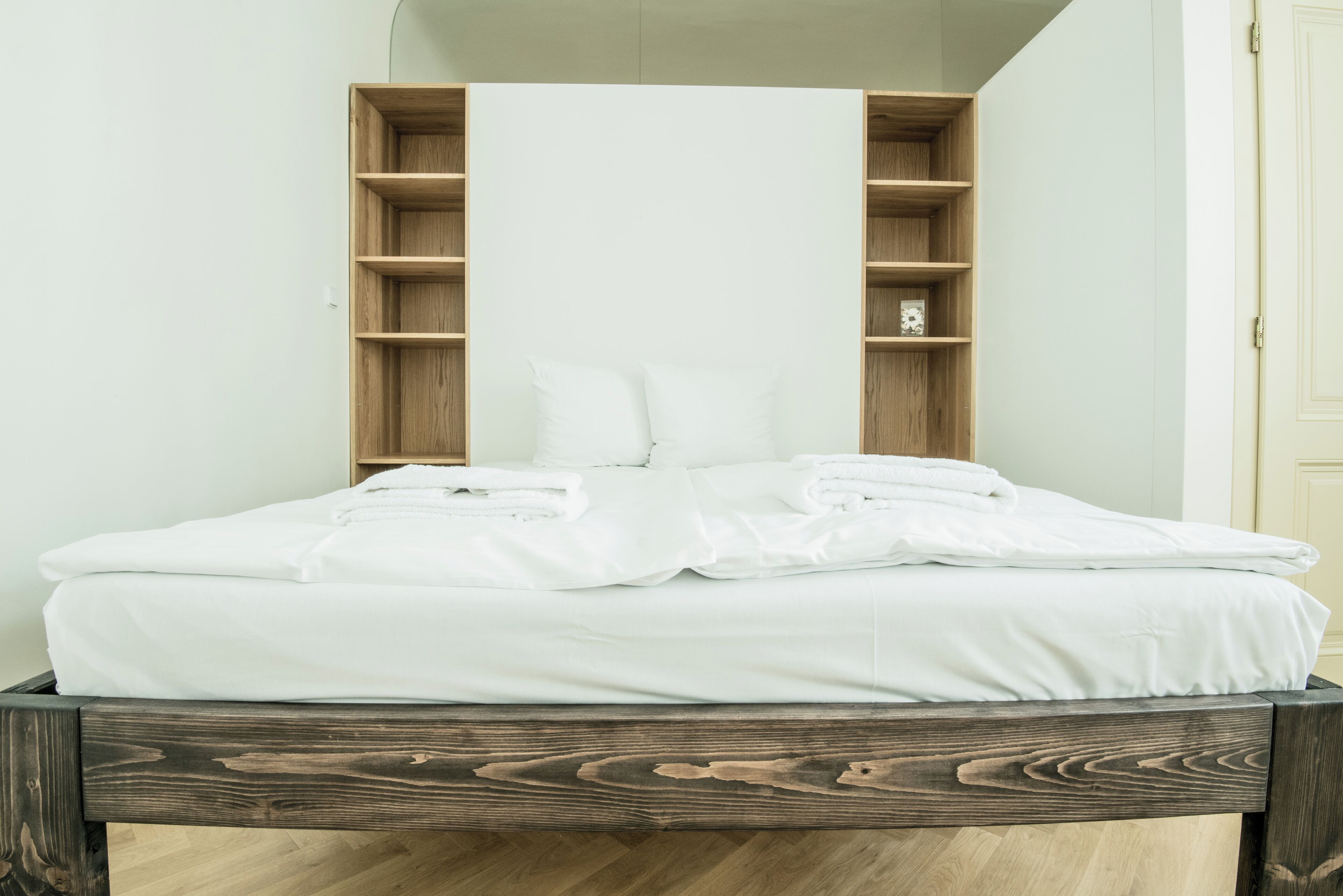 Una cama bien tendida con sábanas y almohadas blancas, cabecera de madera y estanterías empotradas a cada lado.