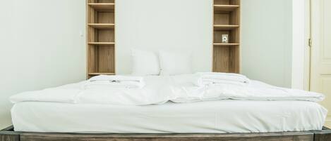 A neatly made bed with white linens and pillows, a wooden headboard, and built-in shelving on either side.