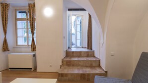 A spacious living area with a staircase leading to a balcony, a white radiator, and a large window with curtains. - Charles Bridge Economic Hostel (Prague)