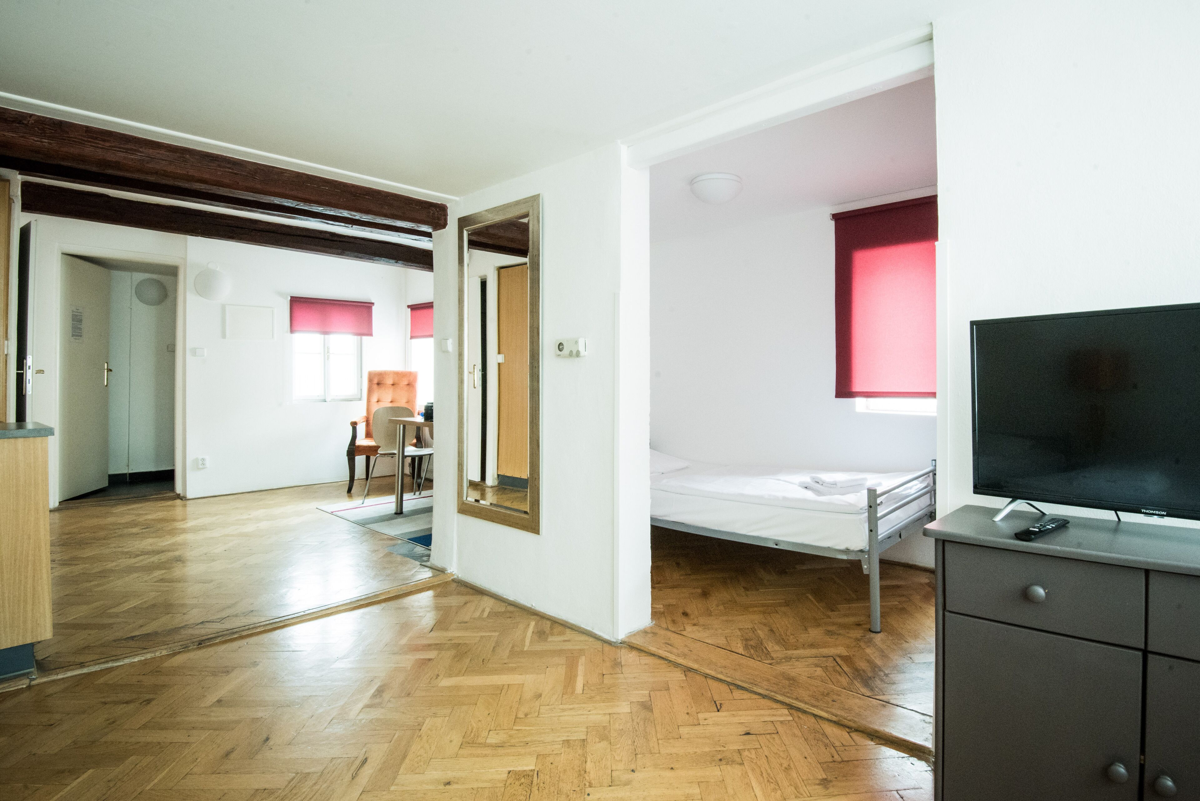 Una stanza con pavimento in legno, un letto, una televisione e una scrivania con cassetti.
